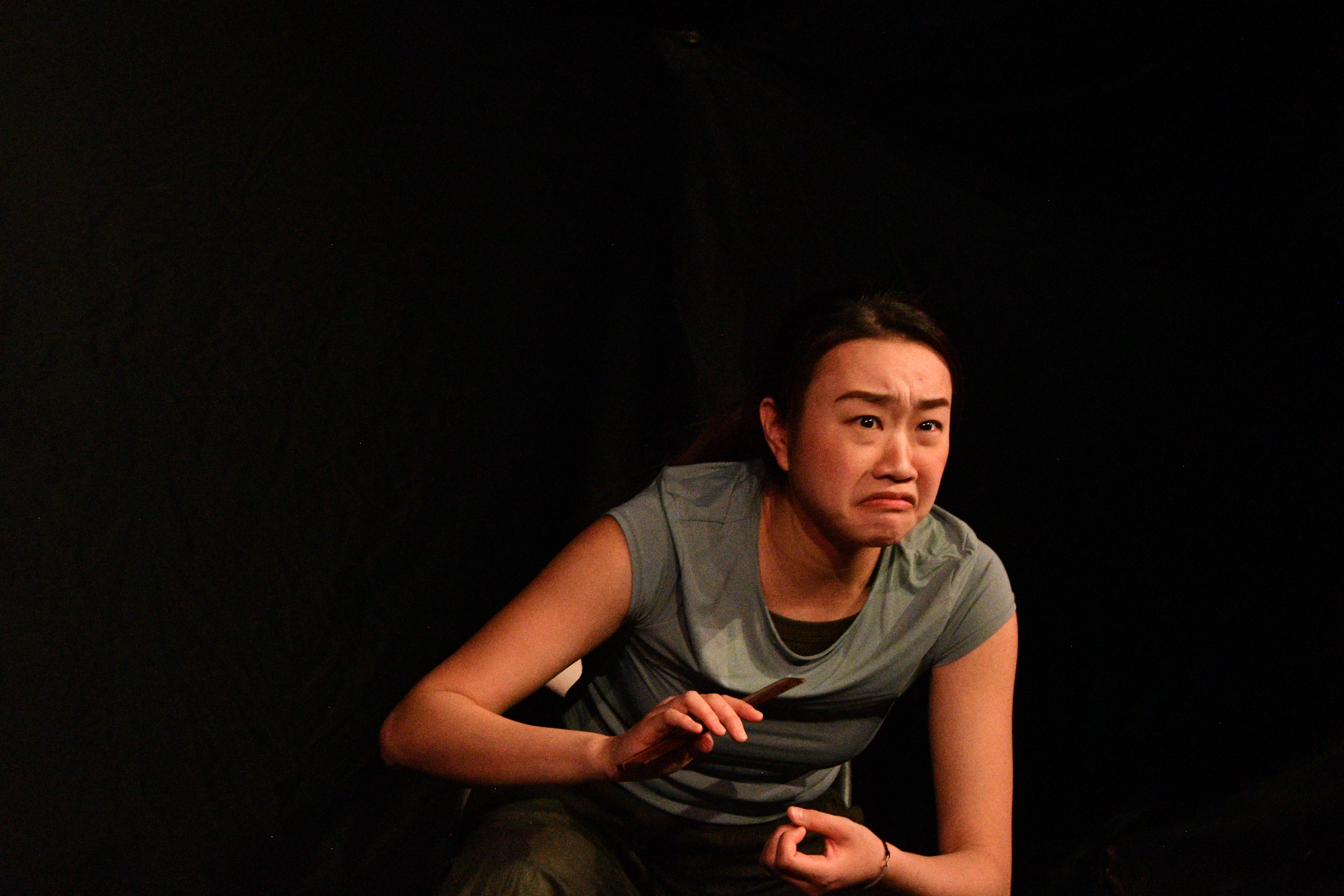 A performer holds a comb, mid-emotion, lit warmly against darkness.