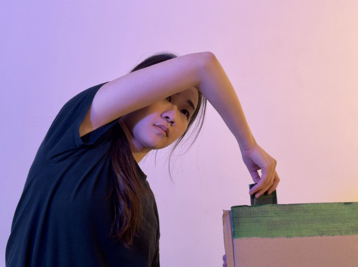 A performer reaches an arm across her face towards a painted cardboard box.