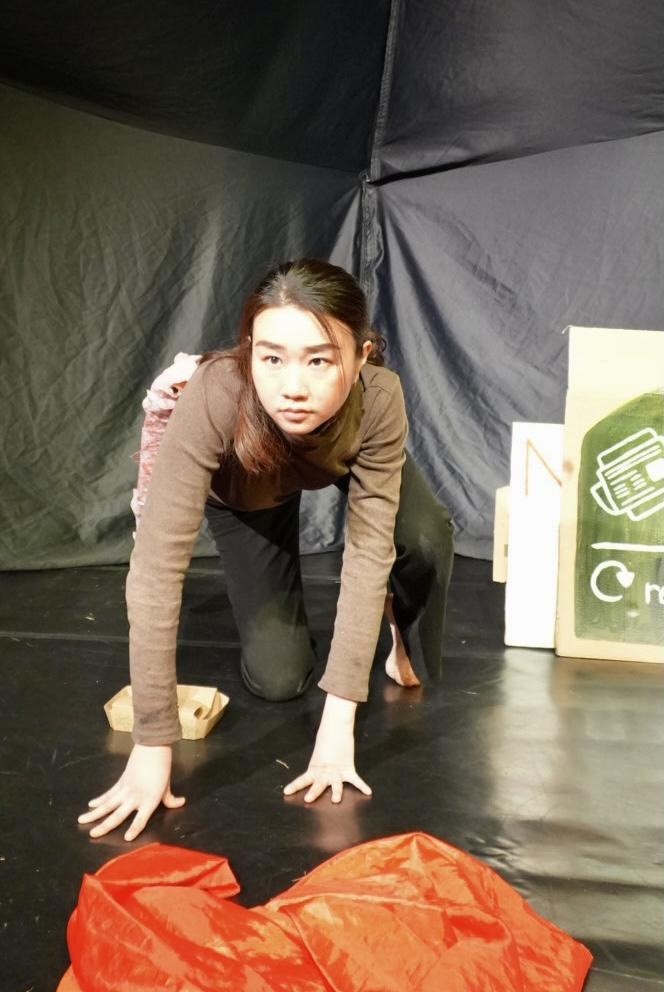 A performer crawls low across the stage, mid-movement, in Out of the Bin.