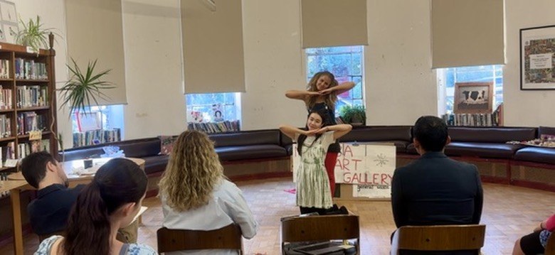 Two performers in a shape together during a library workshop, audience in the foreground.